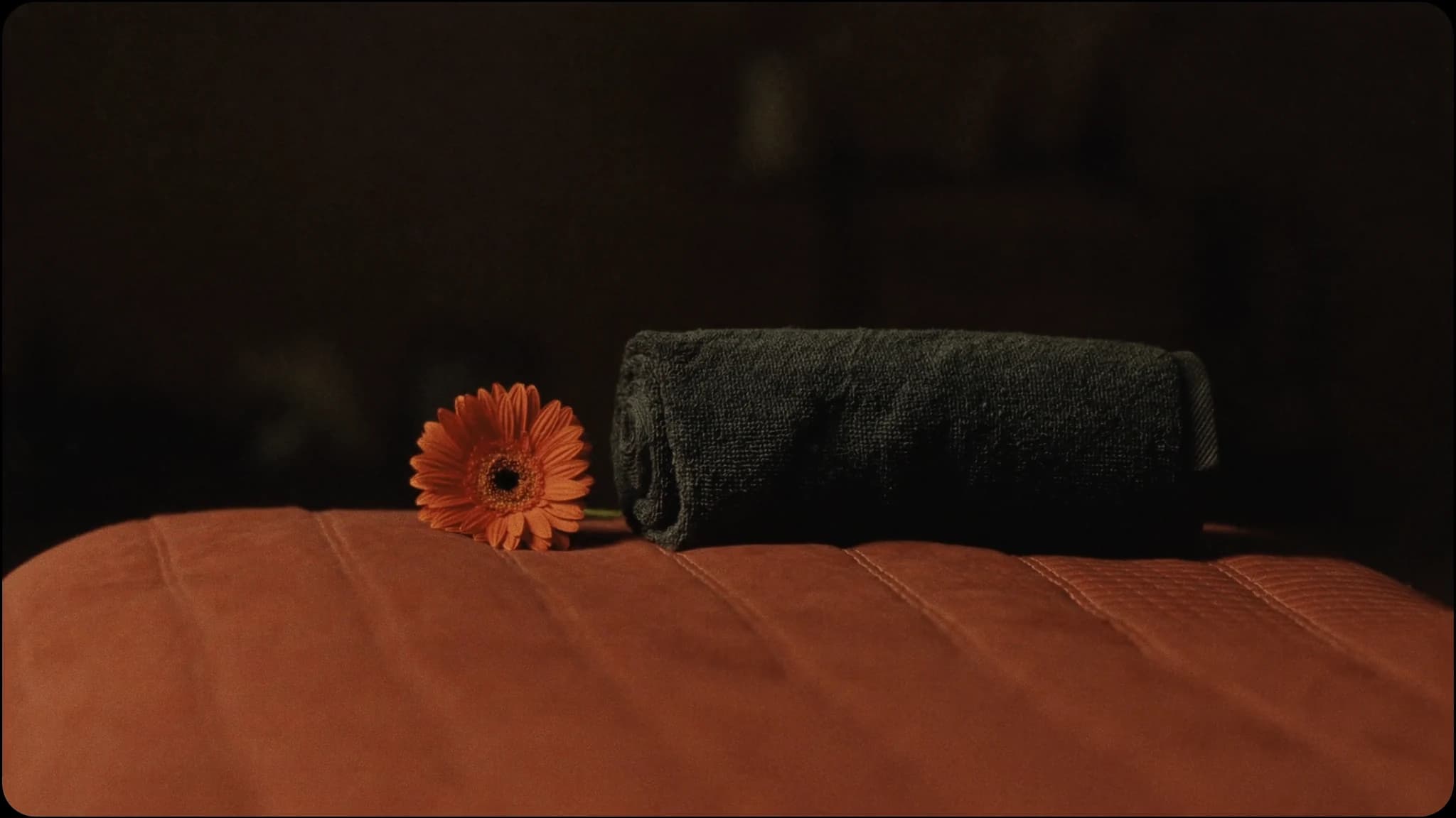 Opgerolde grijze handdoek en een oranje gerbera op de terracotta massagetafel