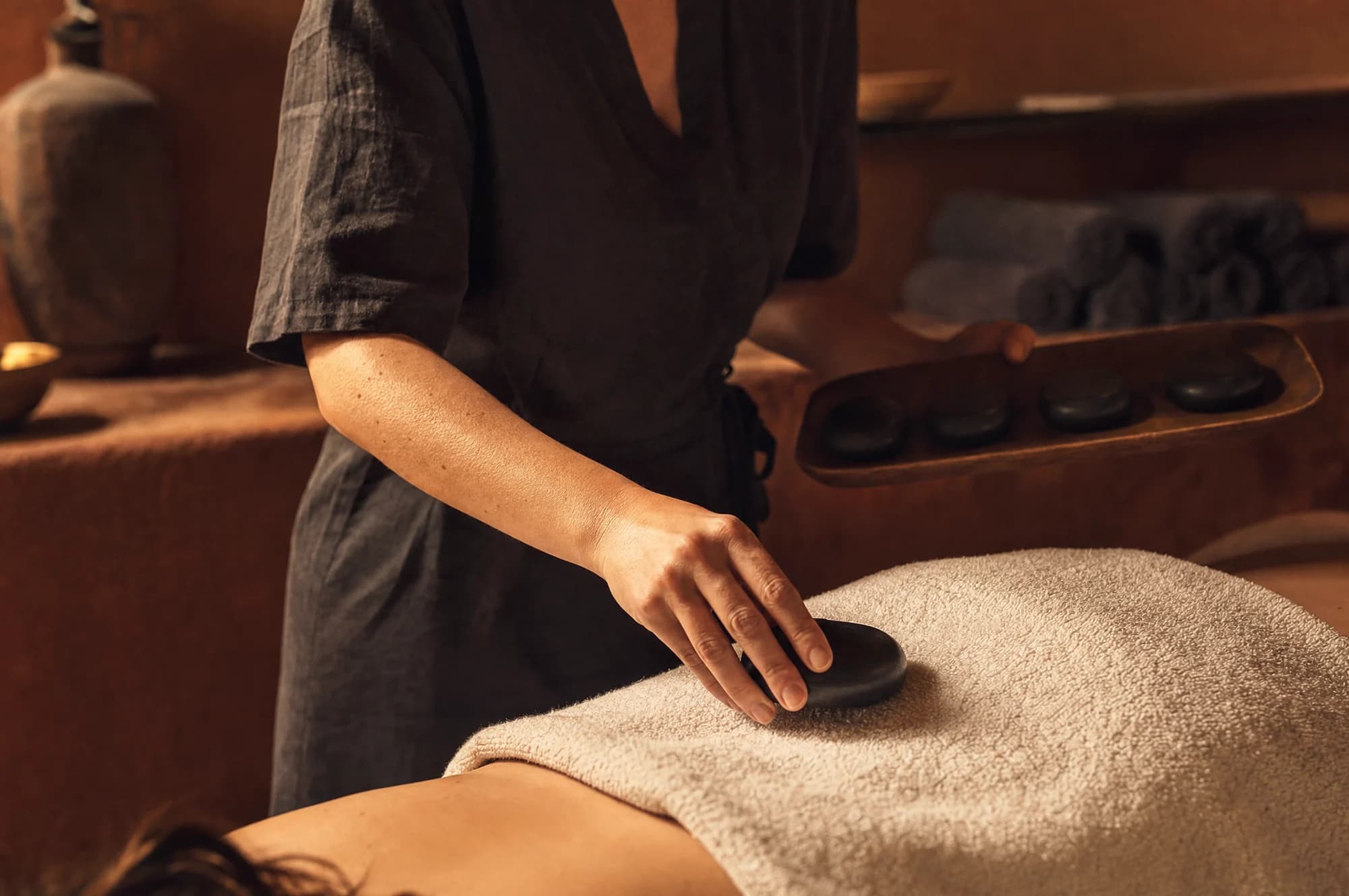 Masseuse die een warme basaltsteen over een handdoek op de rug legt