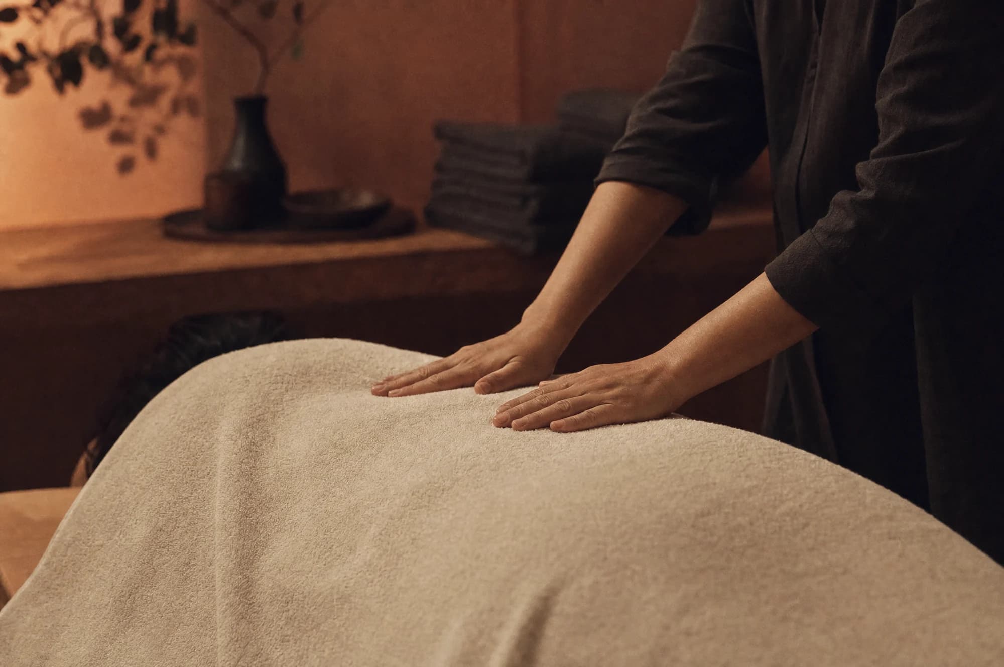 Handen van een masseuse die met vlakke palmen over de rug van een klant onder een handdoek werken